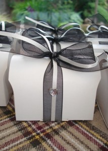Off-white favour boxes filled with home-made tablet & table trivia, decorated with blank ribbon & heart diamante